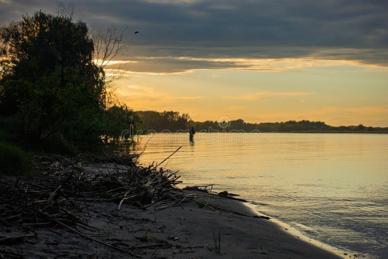 A tranquil evening scene of a fisherman wading in a serene lake at sunset creating warm light royalty free stock photos