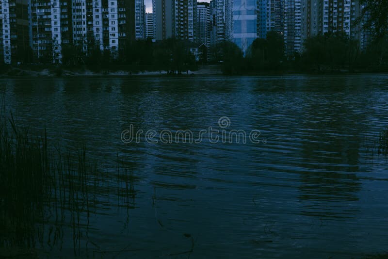 A tranquil evening scene of a lake reflecting city lights, buildings and water creating a mirrored effect at dusk. Reeds stock image