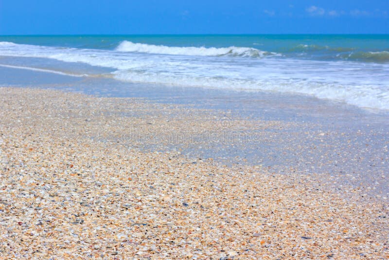 A tranquil sea scene and gravel beach. The sky above is a perfect blue color. Outdoors.