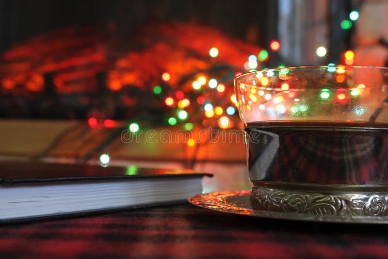 Transparent Cup of tea in a steel Cup holder on the background of a burning fireplace and Christmas garland stock photography Transparent Cup of tea in a steel Cup holder on the background of a burning fireplace and Christmas garland stock photography