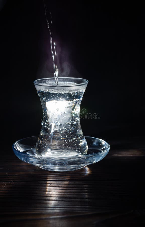 Transparent glass cup with swell the boiling water into it. The vapor from the top. Black background.