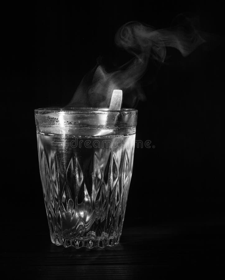 Transparent glass cup with swell the boiling water into it. The vapor from the top. Black background.