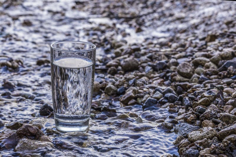 A transparent glass of pure natural cold water stands on a rock in a mountain stream.