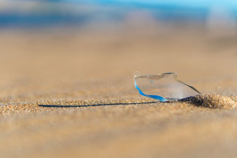 Transparent sharp glass shard from a bottle sticking out of the sand on the beach