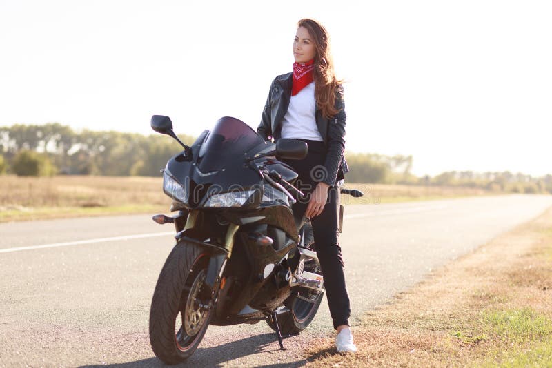 Transport and extreme concept. Thoughtful stylish female motorcyclist enjoys high speed, poses on fast bike, breathes fresh air, c