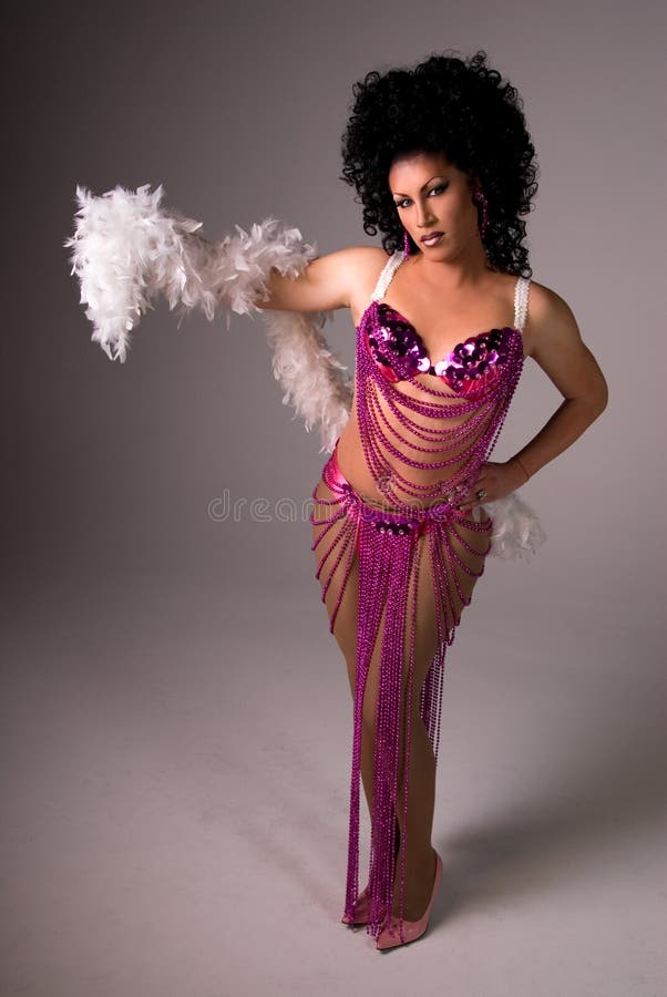 Full length shot of a glamorous Drag queen wearing a pink beaded showgirl costume, with a feather boa draped over her arm. She is looking at the camera. Full length shot of a glamorous Drag queen wearing a pink beaded showgirl costume, with a feather boa draped over her arm. She is looking at the camera.