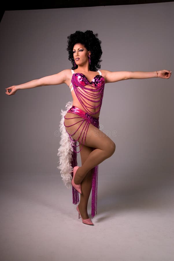 Full length shot of a glamorous Drag queen wearing a pink beaded showgirl costume, with both arms out to the side and standing on one leg. Full length shot of a glamorous Drag queen wearing a pink beaded showgirl costume, with both arms out to the side and standing on one leg.