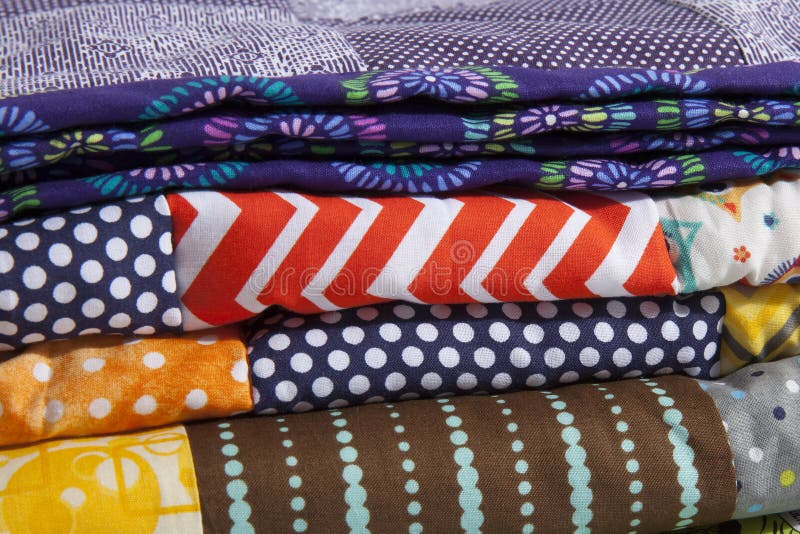 A close up of stacked quilts showing different patterns and cloth texture. A close up of stacked quilts showing different patterns and cloth texture.