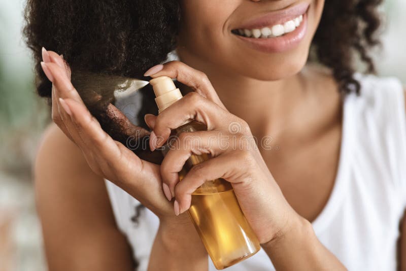 Tratamiento de fin de división. mujer negra sonriente rociando aceite esencial en el pelo rizado fotos de archivo libres de regalías