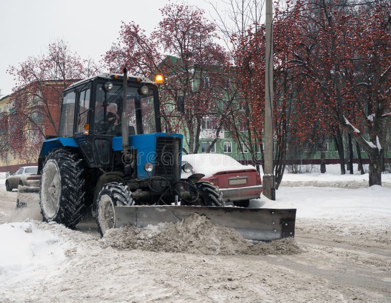 Trator azul que limpa as ruas das grandes quantidades de neve na cidade após a queda de neve Um snowplow que cancela uma estrada fotografia de stock Trator azul que limpa as ruas das grandes quantidades de neve na cidade após a queda de neve Um snowplow que cancela uma estrada fotografia de stock