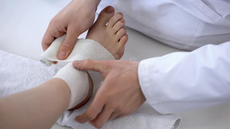 Traumatologist applying bandage to sprained ankle, workout injury, leg closeup