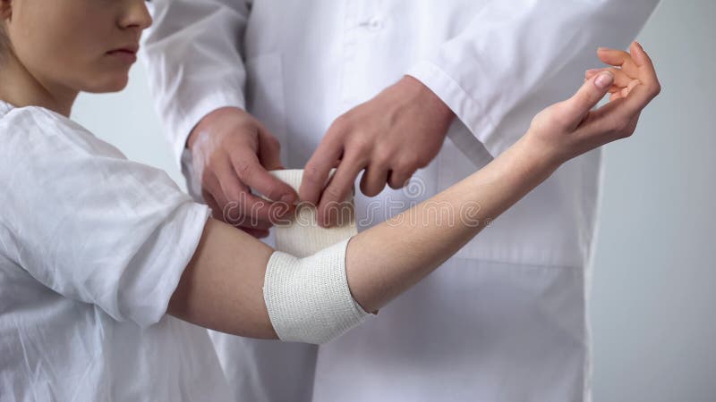 Traumatologist перевязывая терпеливый локоть, скорую помощь для растяжения в клинике травмы стоковое фото rf Traumatologist перевязывая терпеливый локоть, скорую помощь для растяжения в клинике травмы стоковое фото rf