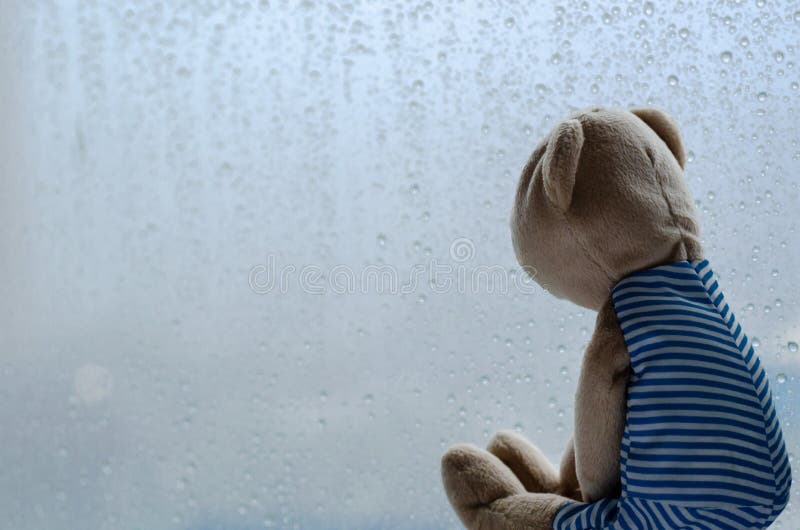 Traurig Teddy Bear, der heraus dem Fenster am regnerischen Tag sitzt und betrachtet