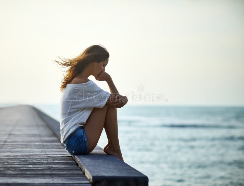 Traurige einsame Schönheit, die auf dem Pier sitzt
