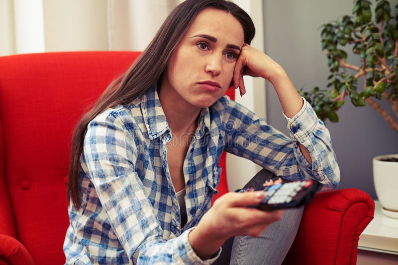 Traurige Frau, die im dem roten Stuhl und dem aufpassenden Fernsehen sitzt stockfoto Traurige Frau, die im dem roten Stuhl und dem aufpassenden Fernsehen sitzt stockfoto