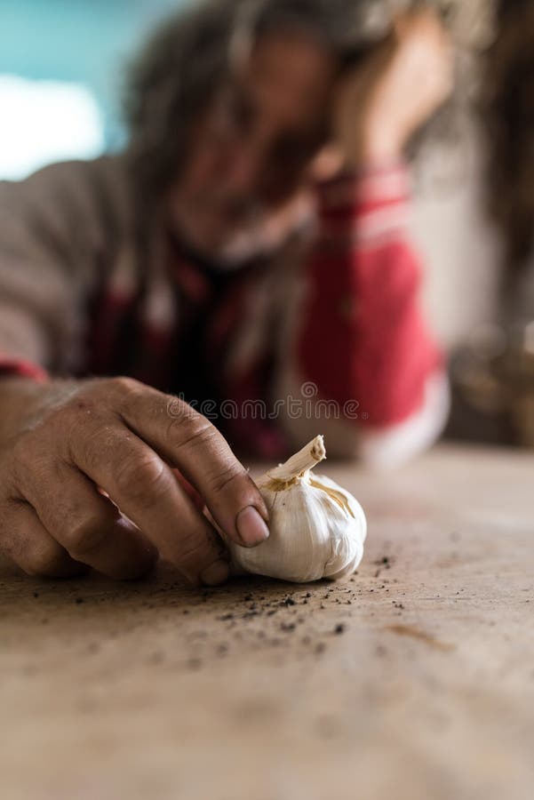 Trauriger Mann, der die Knoblauchknolle hält es mit den beschmutzten Händen betrachtet lizenzfreie stockfotografie Trauriger Mann, der die Knoblauchknolle hält es mit den beschmutzten Händen betrachtet lizenzfreie stockfotografie