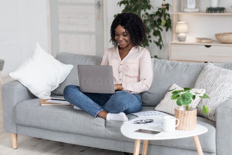 Travail à distance. Femme de couleur joyeuse travaillant sur l'ordinateur portable sur le canapé à la maison image stock