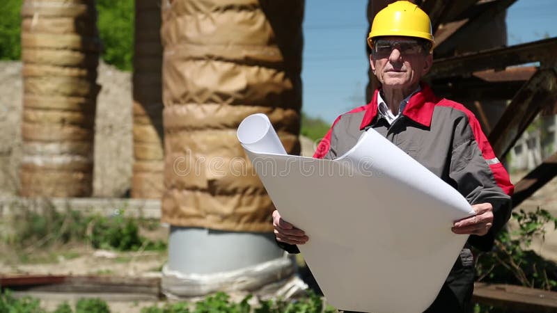 Travailleur dans le casque antichoc jaune avec des dessins d'étude à la station de la chaleur