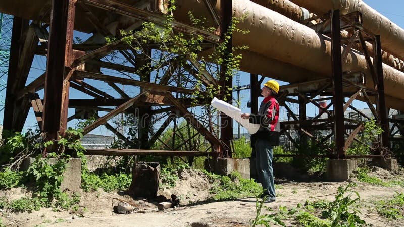 Travailleur dans le casque antichoc jaune avec des dessins de projet à la centrale