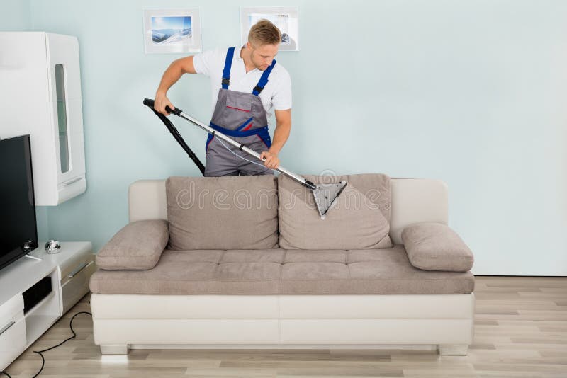Travailleur de sexe masculin nettoyant Sofa With Vacuum Cleaner photographie stock Travailleur de sexe masculin nettoyant Sofa With Vacuum Cleaner photographie stock