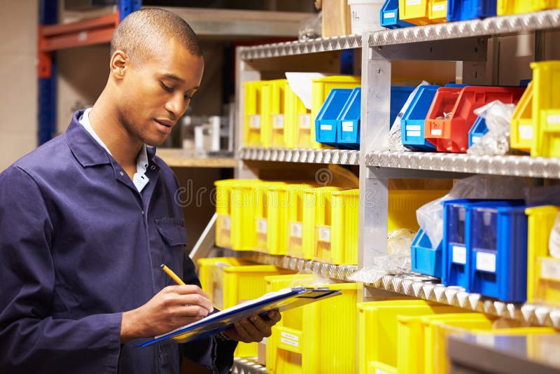 Worker Checking Stock Levels In Store Room Writing Down Information. Worker Checking Stock Levels In Store Room Writing Down Information