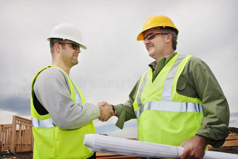Two handsome construction workers shaking hands and smiling on the jobsite. Two handsome construction workers shaking hands and smiling on the jobsite