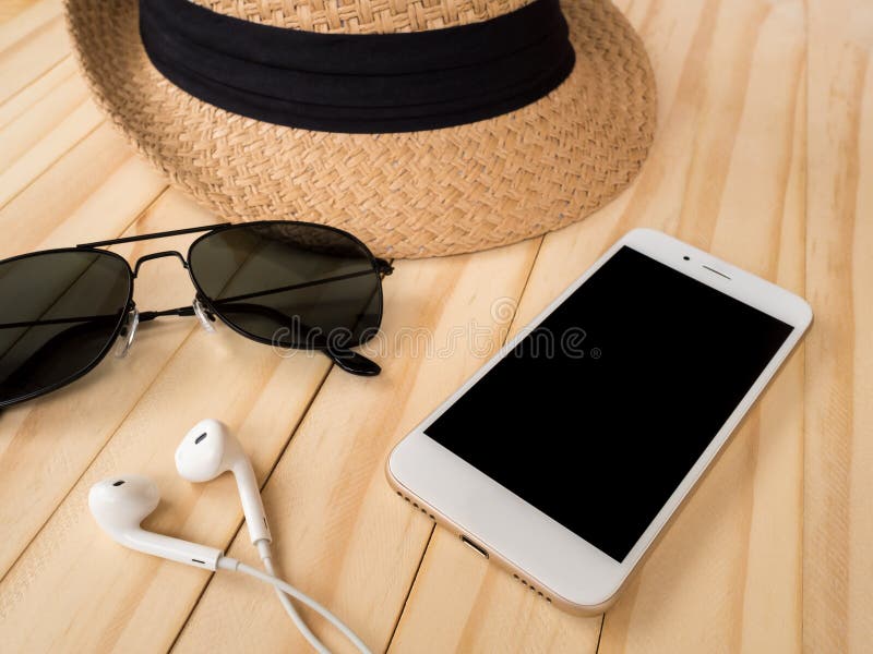 Travel accessories concept. Smartphone, earbuds, sunglasses, woven hat on wooden table. Travel accessories concept. Smartphone, earbuds, sunglasses, woven hat on wooden table.