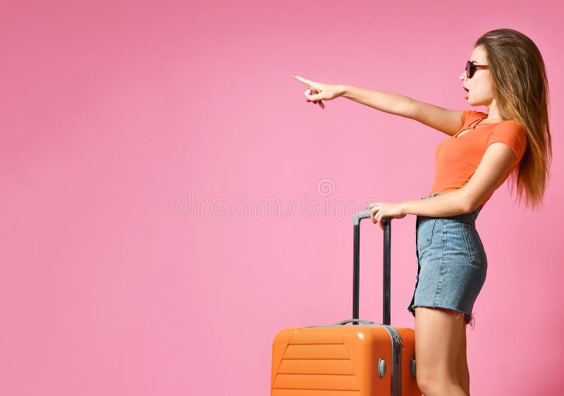 Portrait of a cheerful young caucasian woman dressed in summer clothes, with a suitcase and pointing finger away royalty free stock photo Portrait of a cheerful young caucasian woman dressed in summer clothes, with a suitcase and pointing finger away royalty free stock photo