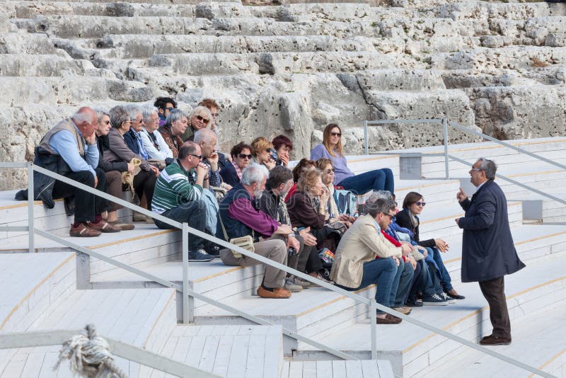 Travel guide with group of tourists sitting on ancient steps