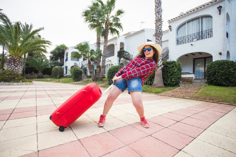 Travel, holidays and people concept - funny woman pulling her heavy suitcase and smiling