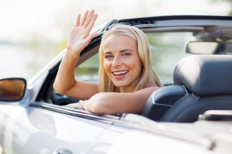 Happy young woman in convertible car waving hand