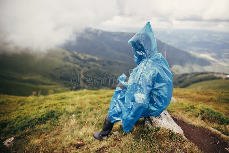 travel and wanderlust concept. traveler hipster girl in blue raincoat with backpack, exploring misty mountains. space for text.