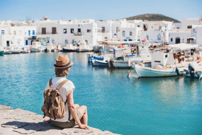 Traveler girl enjoying vacation in Greece. Young woman wearing hat looking at greek village with sea. Summer holidays, vacations