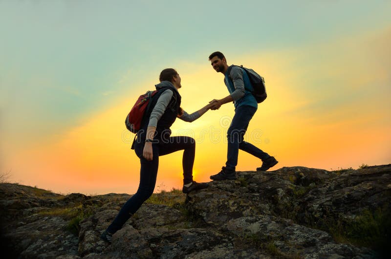 Travelers Hiking in the Mountains at Sunset. Man Helping Woman to Climb to the Top. Family Travel and Adventure.