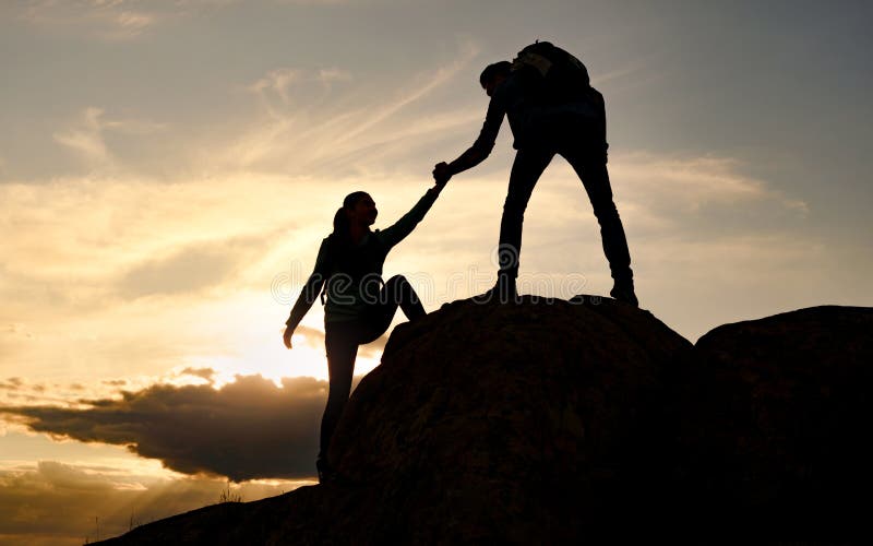 Travelers Hiking in the Mountains at Sunset. Man Helping Woman to Climb to the Top. Family Travel and Adventure.