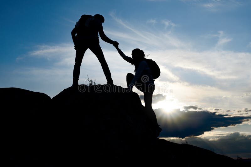 Travelers Hiking in the Mountains at Sunset. Man Helping Woman to Climb to the Top. Family Travel and Adventure.