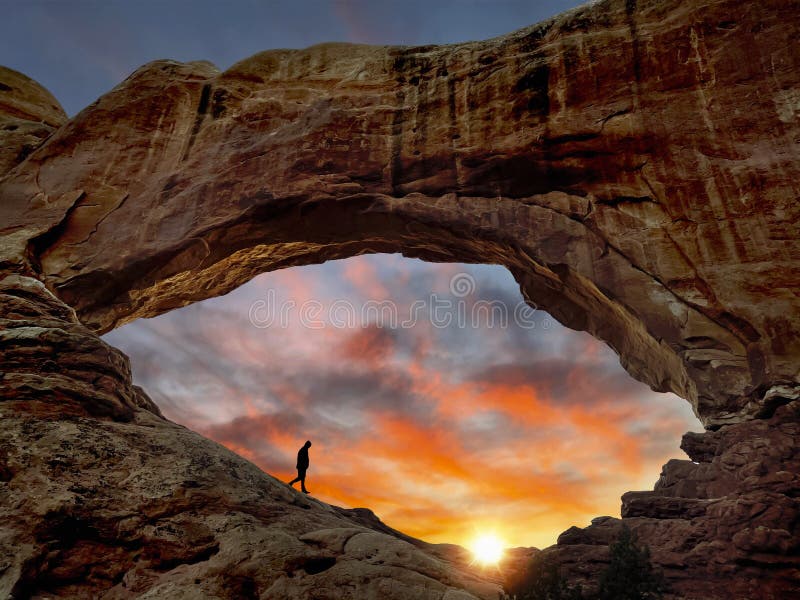 A traveller hiking a beautiful desert scenic landscape during sunrise or sunset North Window arch at Arches National Park in Utah. A beautiful colorful sky and