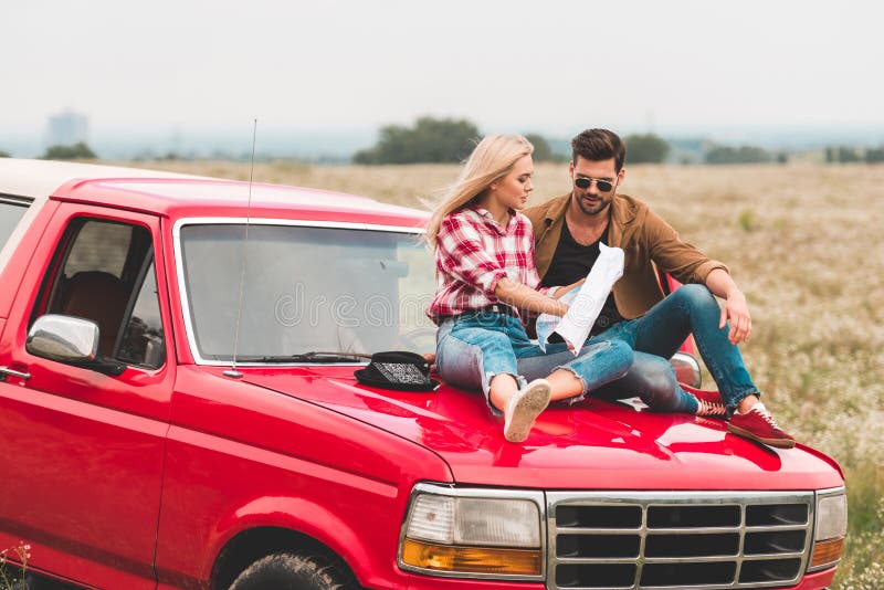 Videos. travelling young couple sitting on car engine hood and navigating. 