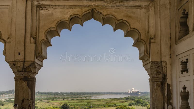 Through the openwork arched vault of the Musamman Burj Palace in the Red Fort, you can see the green valley, the lake and the beautiful Taj Mahal in the distance. India. Agra. Through the openwork arched vault of the Musamman Burj Palace in the Red Fort, you can see the green valley, the lake and the beautiful Taj Mahal in the distance. India. Agra