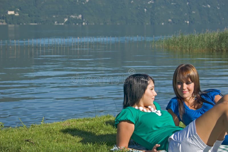 2 young woman lengthened in the grass at the edge of a lake. 2 young woman lengthened in the grass at the edge of a lake