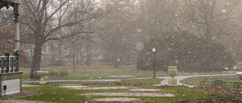 Trayectoria y bancos vacíos en jardines públicos durante ráfaga de nieve con la charca en fondo imagen de archivo Trayectoria y bancos vacíos en jardines públicos durante ráfaga de nieve con la charca en fondo imagen de archivo