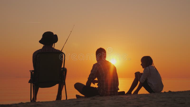 Tre adolescenti stanno pescando sulla riva del lago al tramonto Concetto felice di infanzia fotografia stock Tre adolescenti stanno pescando sulla riva del lago al tramonto Concetto felice di infanzia fotografia stock