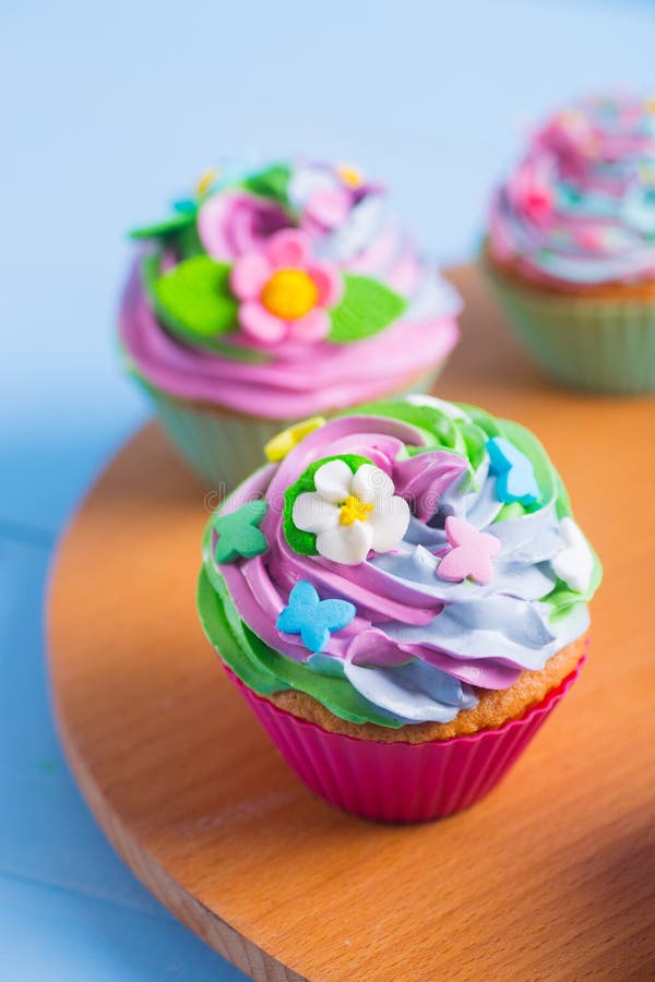 Tre bigné teneri con superiore multicolore cremoso decorati con i fiori variopinti e le farfalle sullo scrittorio rotondo di legn fotografie stock libere da diritti Tre bigné teneri con superiore multicolore cremoso decorati con i fiori variopinti e le farfalle sullo scrittorio rotondo di legn fotografie stock libere da diritti
