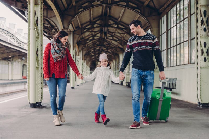 Tre familjemedlemmar på järnvägsstation Den lyckliga modern, dottern och fadern har positiva ansiktsuttryck, väntar på på drevet royaltyfri fotografi Tre familjemedlemmar på järnvägsstation Den lyckliga modern, dottern och fadern har positiva ansiktsuttryck, väntar på på drevet royaltyfri fotografi