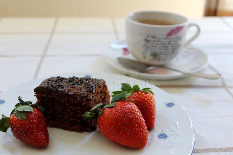 Tre fragole rosse fresche intorno ad un dolce di cioccolato delizioso e saporito e ad una tazza di caffè a fondo fotografia stock Tre fragole rosse fresche intorno ad un dolce di cioccolato delizioso e saporito e ad una tazza di caffè a fondo fotografia stock