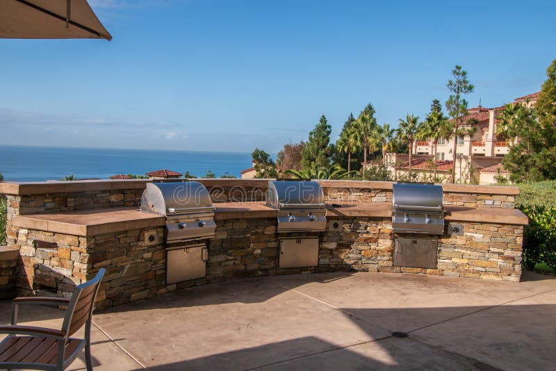 Tre gasgrillfestgaller som byggs in i en stenvägg på en uteplats som förbiser havet och en semesterort royaltyfria foton Tre gasgrillfestgaller som byggs in i en stenvägg på en uteplats som förbiser havet och en semesterort royaltyfria foton