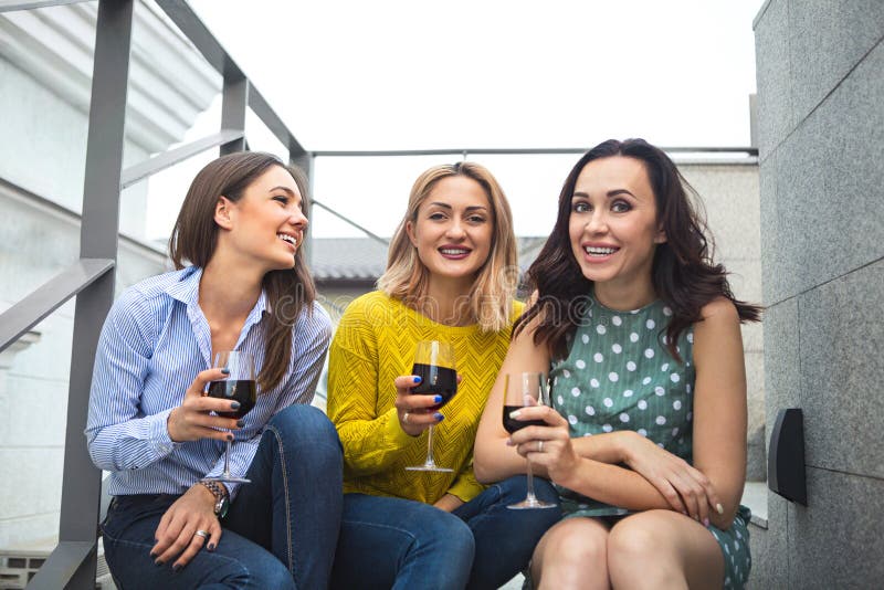 Tre giovane donna felice che ride, vino rosso bevente, divertendosi fotografie stock Tre giovane donna felice che ride, vino rosso bevente, divertendosi fotografie stock