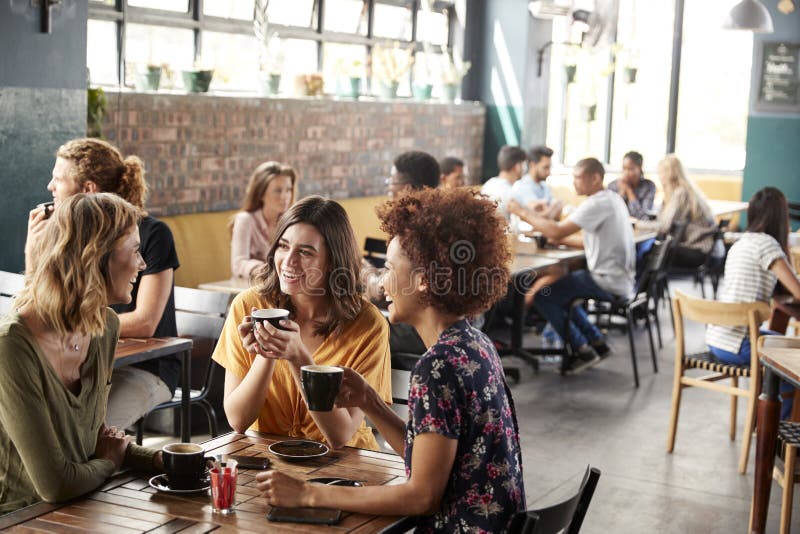 Tre giovani amici femminili che incontrano il negozio e conversazione di Sit At Table In Coffee