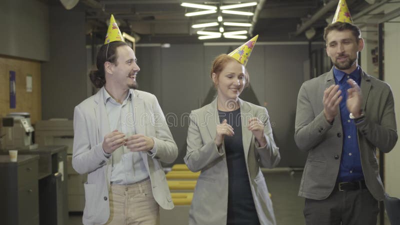 Tre kaukasiska kontorsanställda i partigrupper dansar i en korridor för arbetsutrymmen Kolleger som har kul på företag