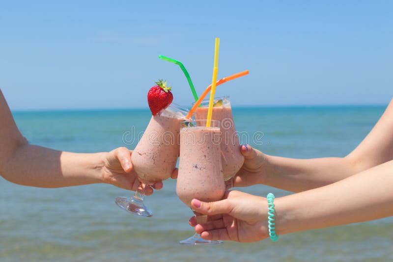 Tre kvinnliga händer rymmer jordgubbemilkshakar på bakgrunden av havet royaltyfri fotografi Tre kvinnliga händer rymmer jordgubbemilkshakar på bakgrunden av havet royaltyfri fotografi
